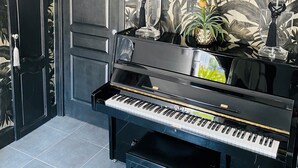 Ein schwarzes Flügel in einem Raum mit tropischem Wandpapier, einer Tür und einem kleinen Hocker.