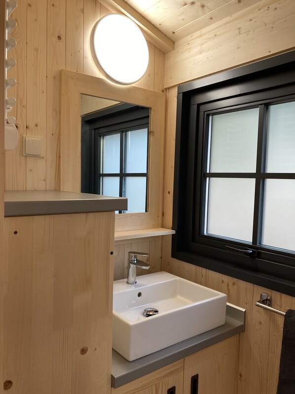 A wooden cabin bathroom with a white sink, a mirror, and a window.