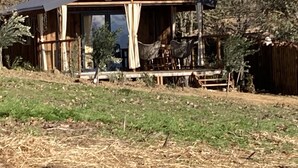 A rustic cabin with a wooden exterior, a covered porch, and a small garden area. - Cabane Insolite et Nature Avec Jacuzzi et Piscine Prés Carcassonne Occitanie (VILLARZEL DU RAZES)