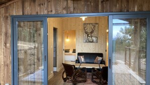 A wooden cabin with a glass door leading to a cozy interior featuring a bed, a sofa, and a deer artwork. - Cabane Insolite et Nature Avec Jacuzzi et Piscine Prés Carcassonne Occitanie (VILLARZEL DU RAZES)