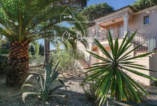 A residential property with a garden, palm trees, and a building with a balcony.