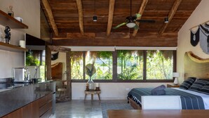 Une cuisine moderne avec un plafond en bois, une grande fenêtre donnant sur un paysage verdoyant et un lit avec une literie à rayures.