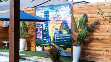 Une clôture en bois ornée d’une fresque colorée, une petite piscine et des plantes en pot.