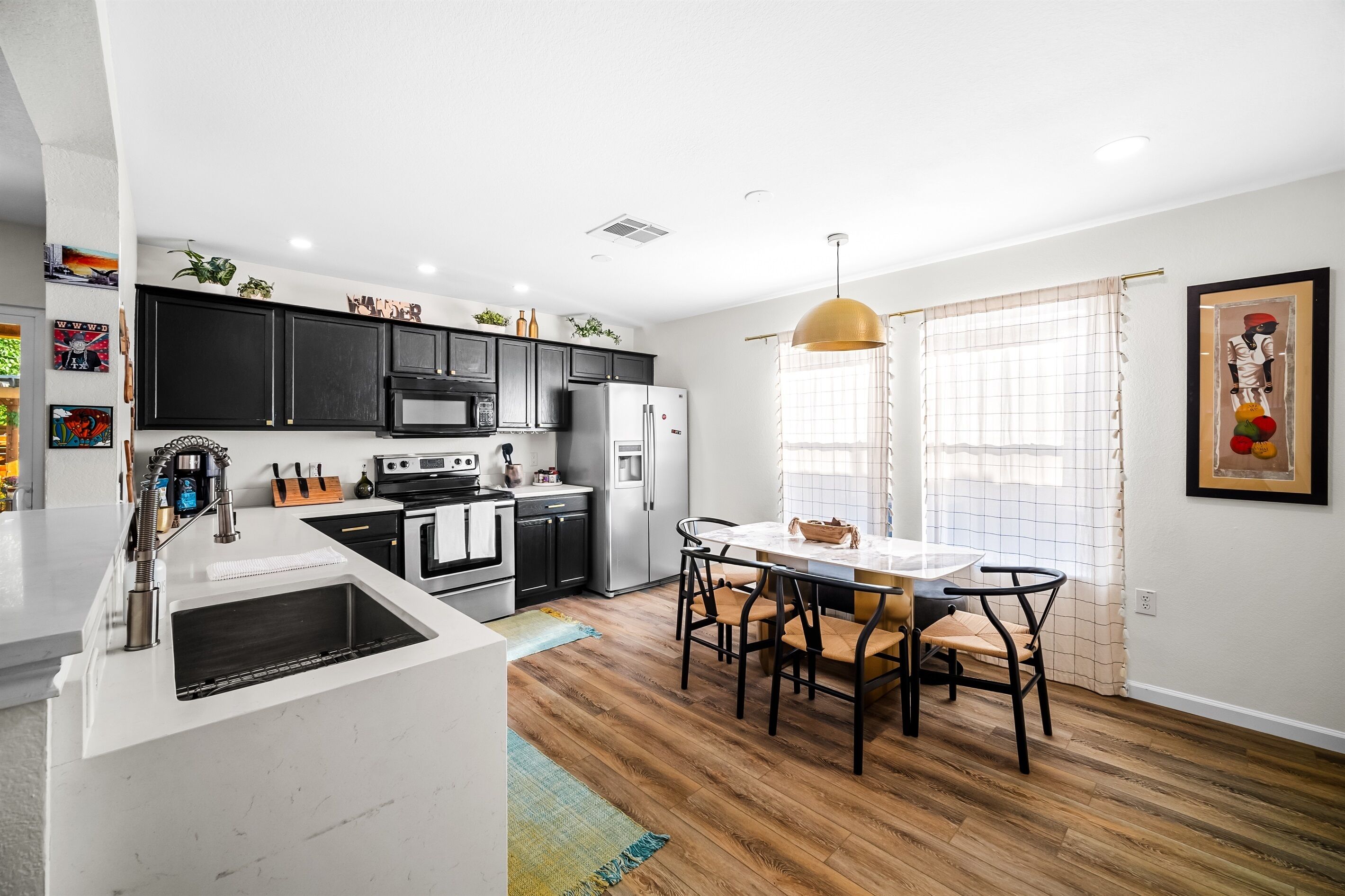 A modern kitchen with black cabinets, a white countertop, and a dining area with a table and chairs.
