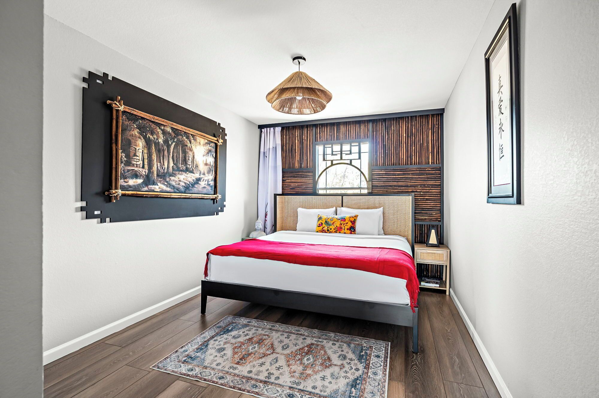 Ein Schlafzimmer mit einem Bett, einer Hängeleuchte, einem Fenster mit Holzlamellen und einem gerahmten Bild an der Wand.