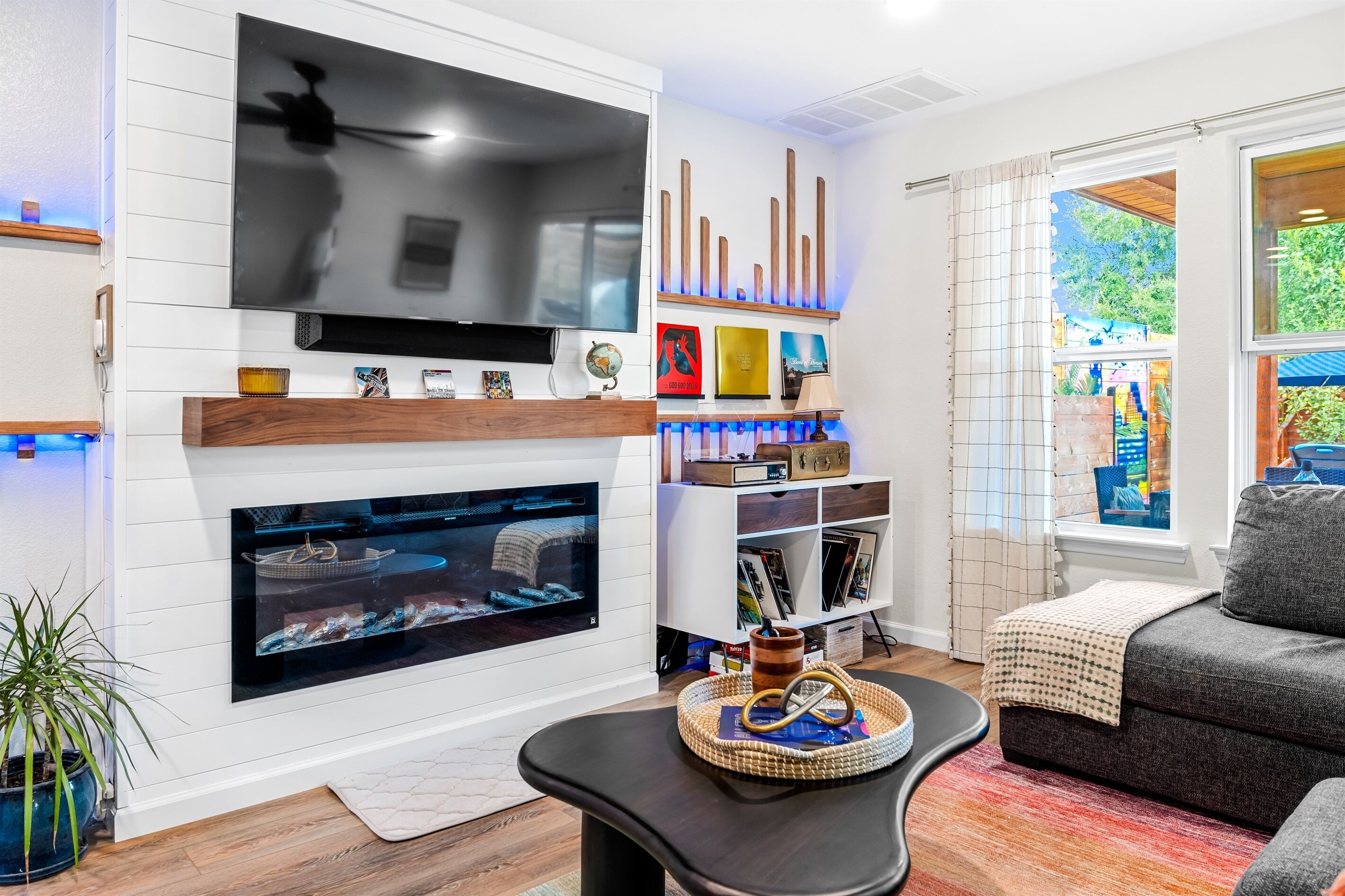 Una sala de estar con televisor de pantalla plana, chimenea, estantería y ventana con vistas al exterior.