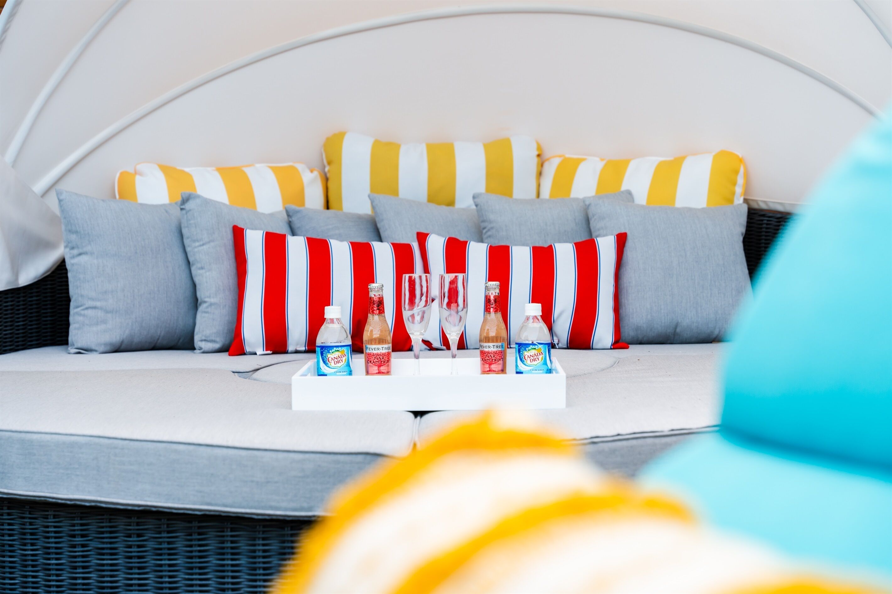 A modern outdoor seating area with a white cushioned bench, striped pillows, and a tray with drinks and glasses.