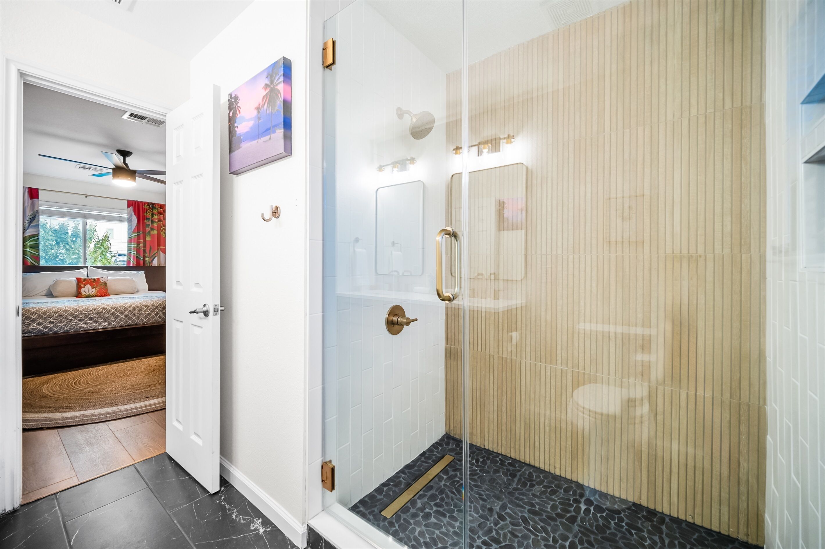 A modern bathroom with a glass shower enclosure, a wooden vanity, and a small seating area with a view of the outdoors.