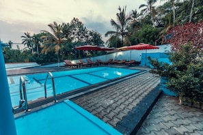 A swimming pool with lounge chairs and umbrellas, surrounded by palm trees and a blue building. - Tropical Paradise Villa in Talpe (Unawatuna)