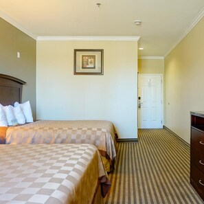 A hotel room with two beds, a framed picture on the wall, a door, and a dresser. - Harbor Inn And Suites (Garden Grove)