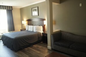 A hotel room with a double bed, a bedside table with a lamp, a sofa, and a framed picture on the wall. - Harbor Inn And Suites (Garden Grove)