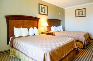 A hotel room with two beds, a nightstand, a lamp, and framed pictures on the walls. - Harbor Inn And Suites (Garden Grove)