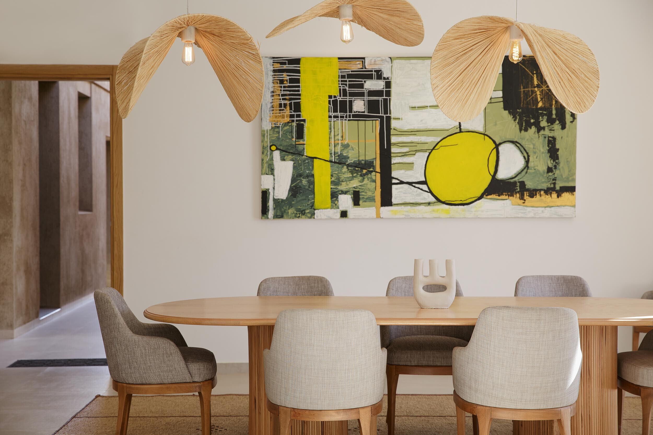 A modern dining area with a wooden table and six chairs, a large abstract painting on the wall, and a unique ceiling light fixture.
