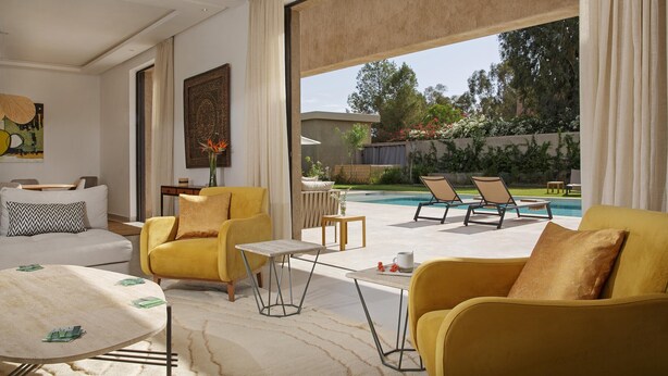 A modern living room with a pool view, featuring yellow sofas, a white coffee table, and a large window. - PEPE, luxury and modern villa with private pool (5 bdrms/10 guests) (Marrakech)