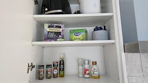 A kitchen pantry with shelves containing Twinings Earl Grey tea, Tetley green tea, and various condiments like black pepper, extra virgin olive oil, and salt. - Studio Flat in Lovely Alexandra Palace, London (London)