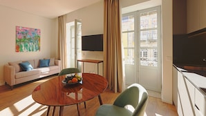 A modern living room with a sofa, a dining table with chairs, a flat-screen TV, and a window with curtains. - RIBEIRA FLORES 59 Downtown Apartments (Porto)