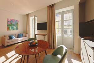 A modern living room with a sofa, a dining table with chairs, a flat-screen TV, and a window with curtains.