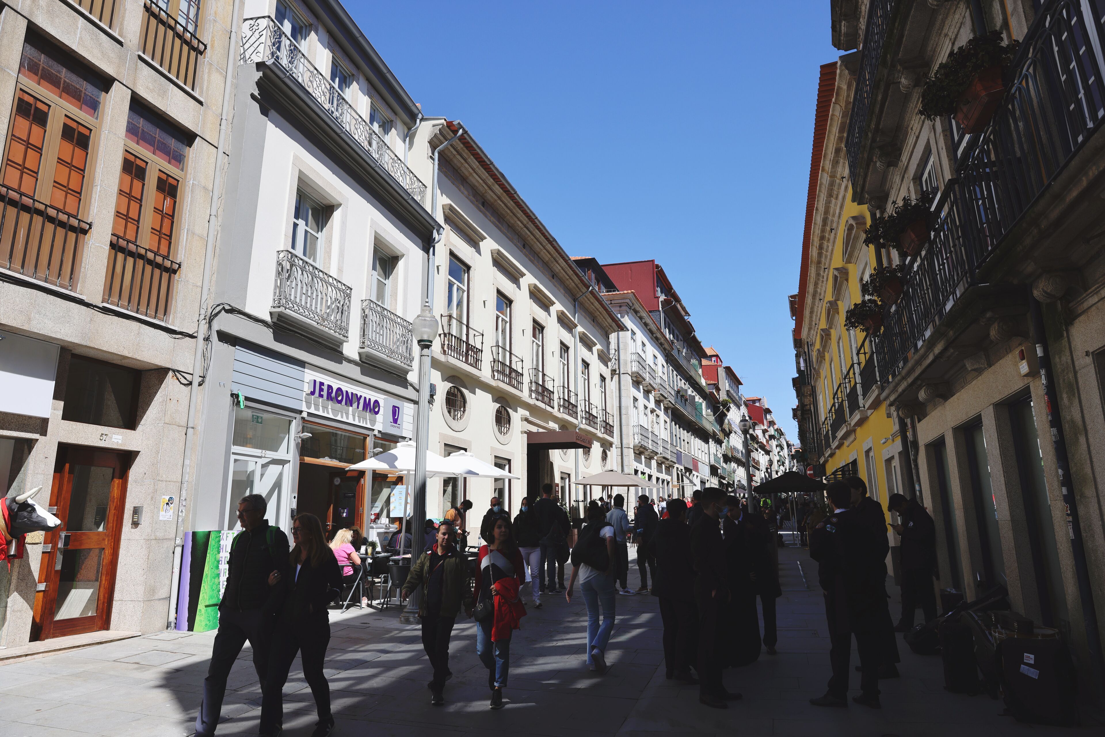 A pedestrian street lined with multi-story buildings, some with balconies and outdoor seating.