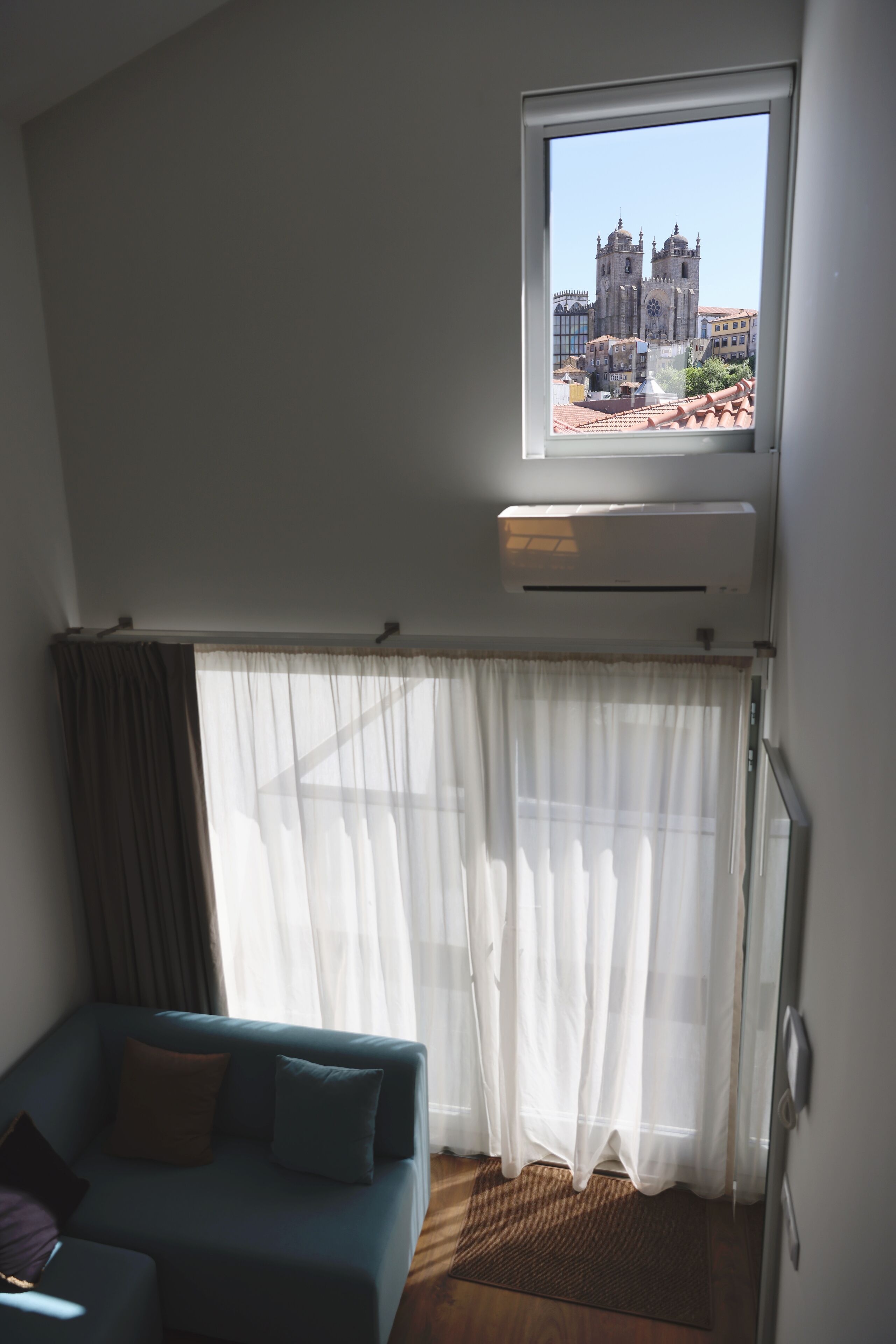 A room with a view of a cathedral through a window, a sofa, and an air conditioning unit.