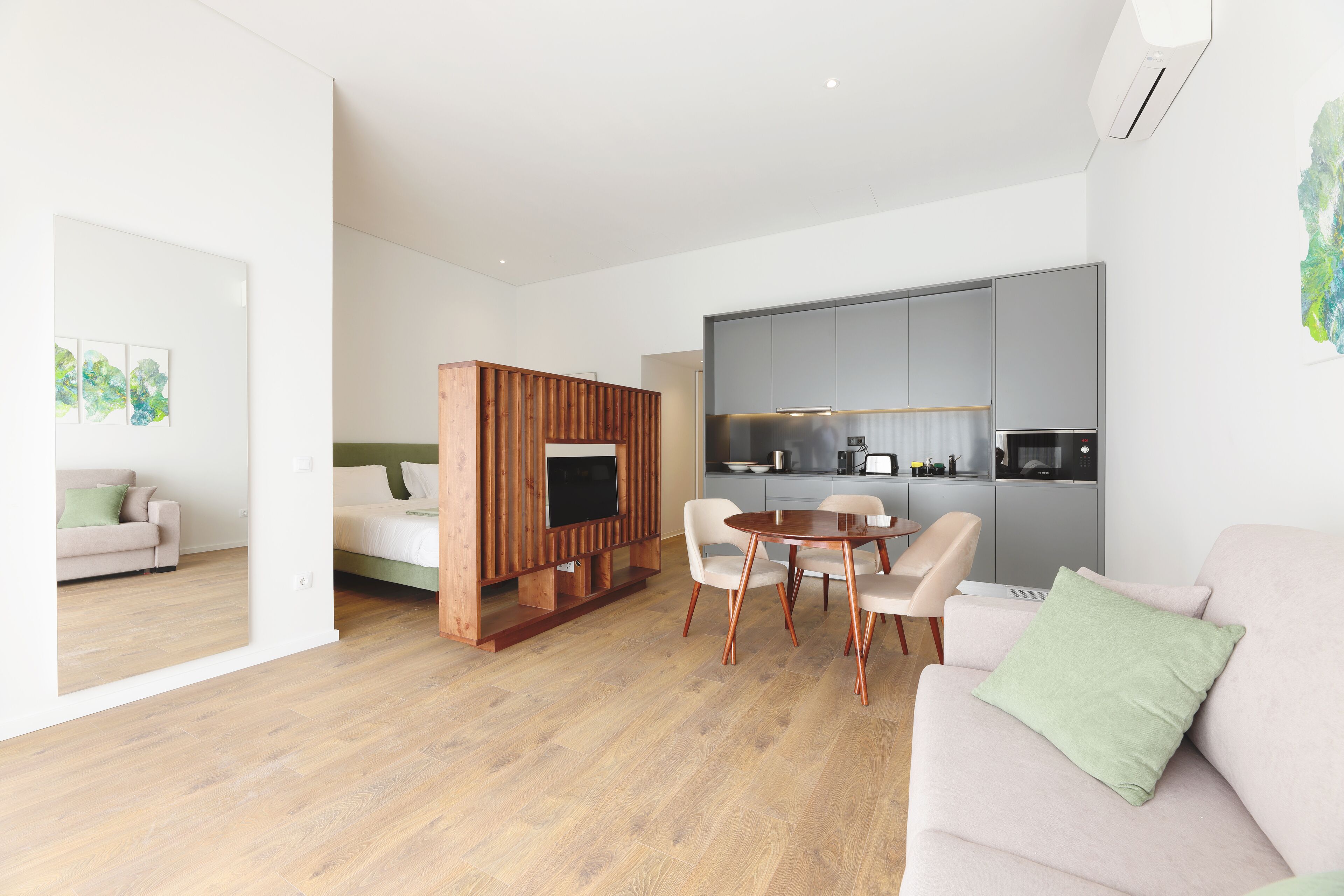 Un soggiorno moderno con un mobile TV in legno, un'area pranzo con un tavolo rotondo e sedie, e una piccola cucina sullo sfondo.