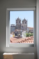 Blick durch ein Fenster auf ein historisches Gebäude mit einem Uhrturm, angrenzende Bauten und ein Ziegeldach.