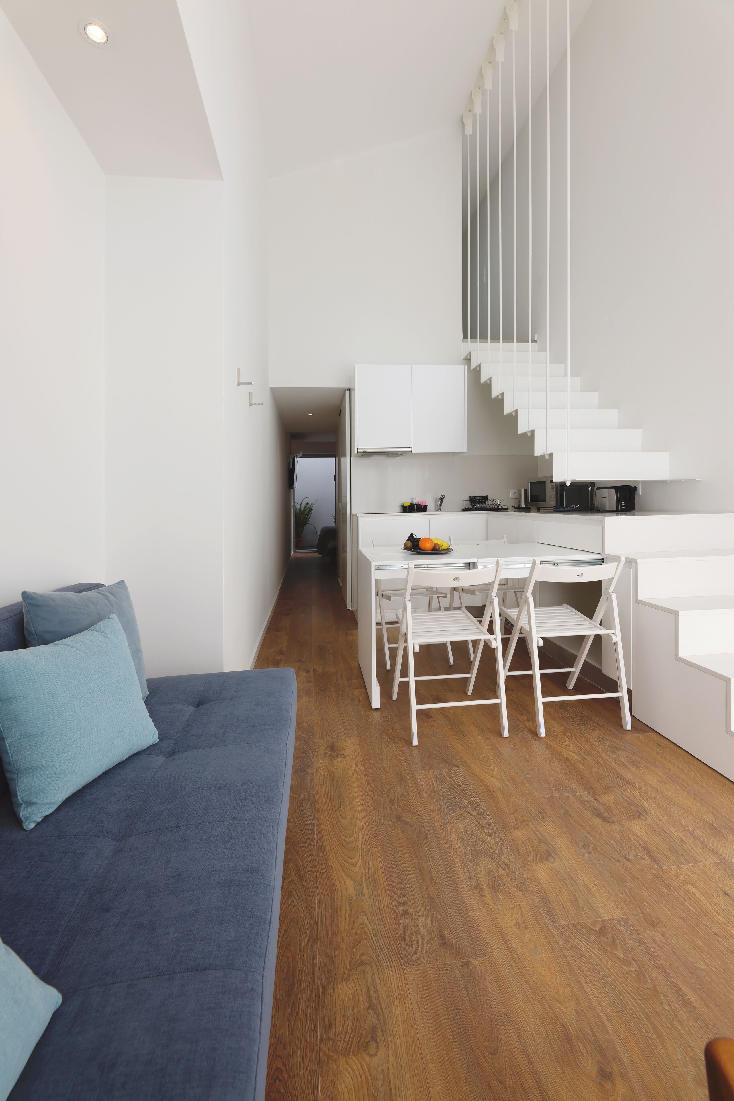 A modern kitchen with white cabinetry, a dining area with a table and chairs, and a staircase leading to another level.