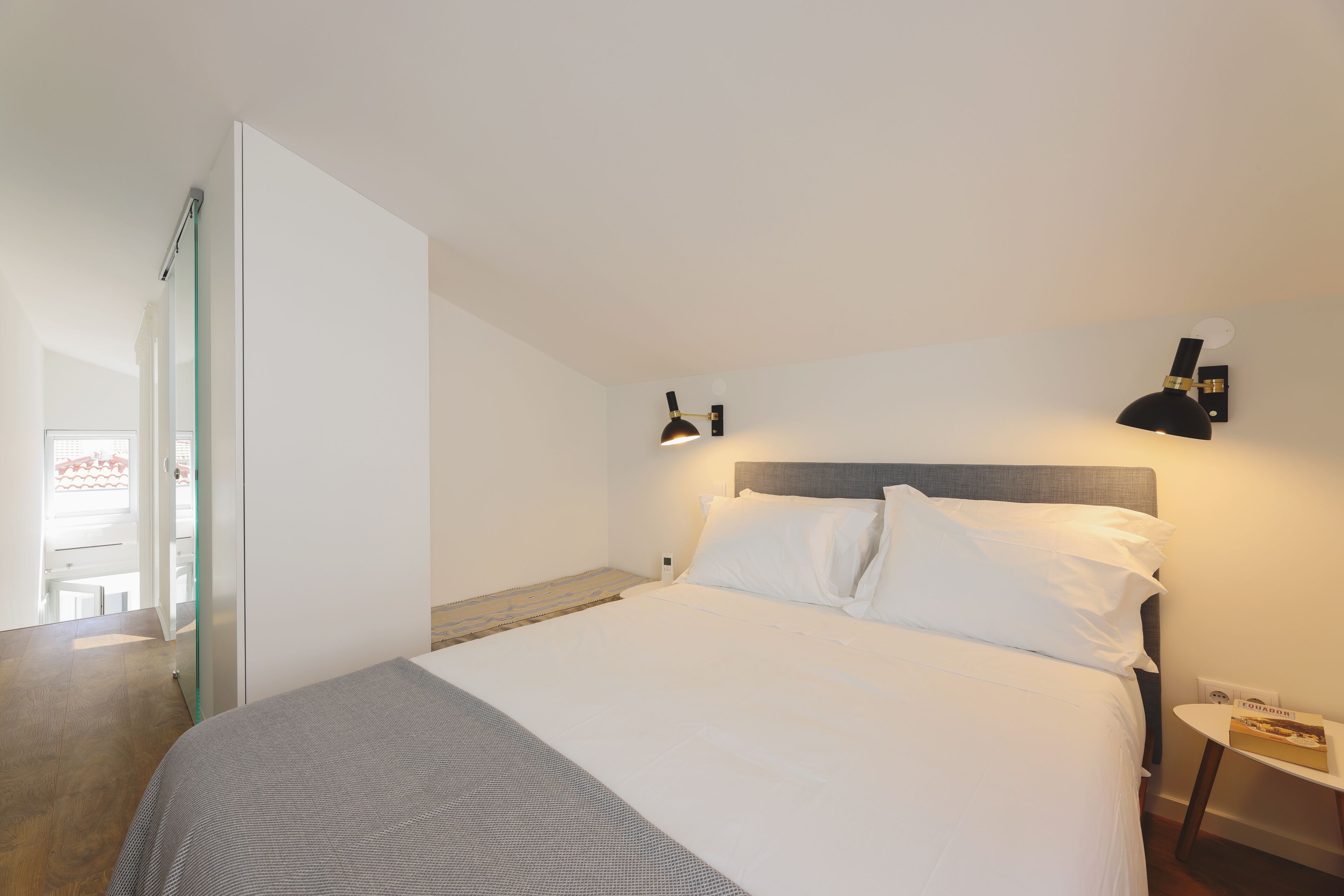A bedroom with a bed, bedside table, and wall-mounted lamp.