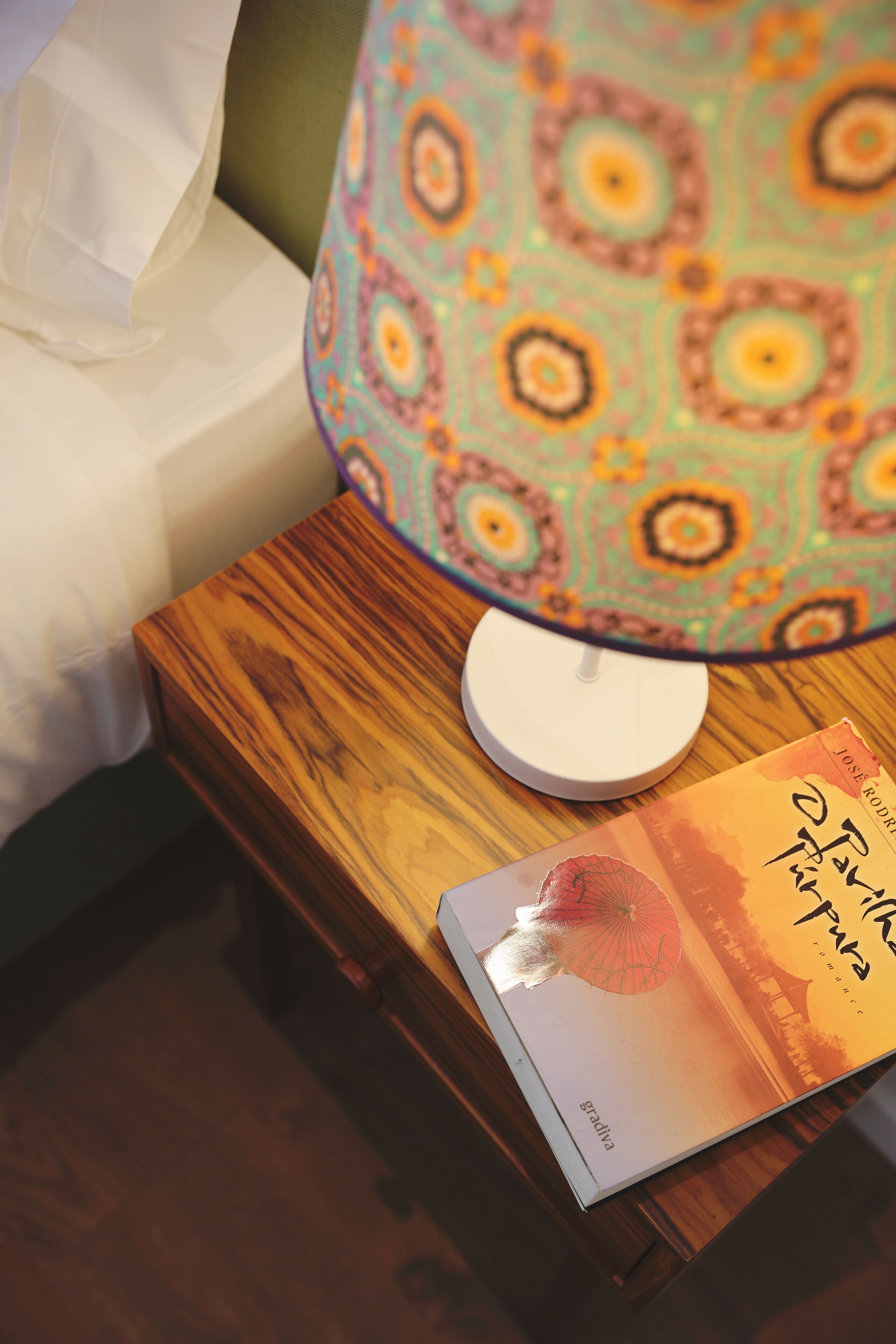 Un comodino con una lampada, un libro e una candela bianca.