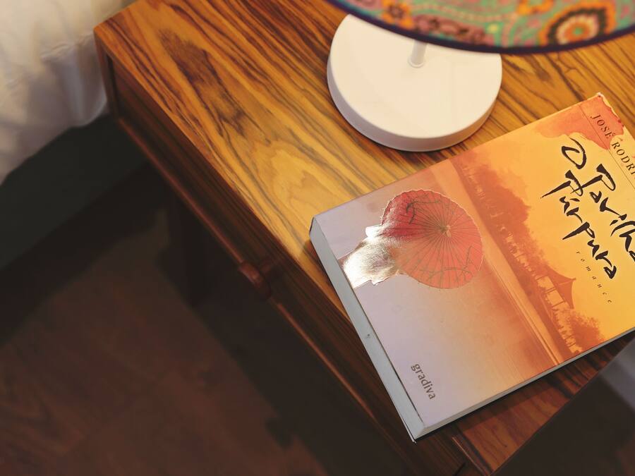 Un comodino con una lampada, un libro e una candela bianca.