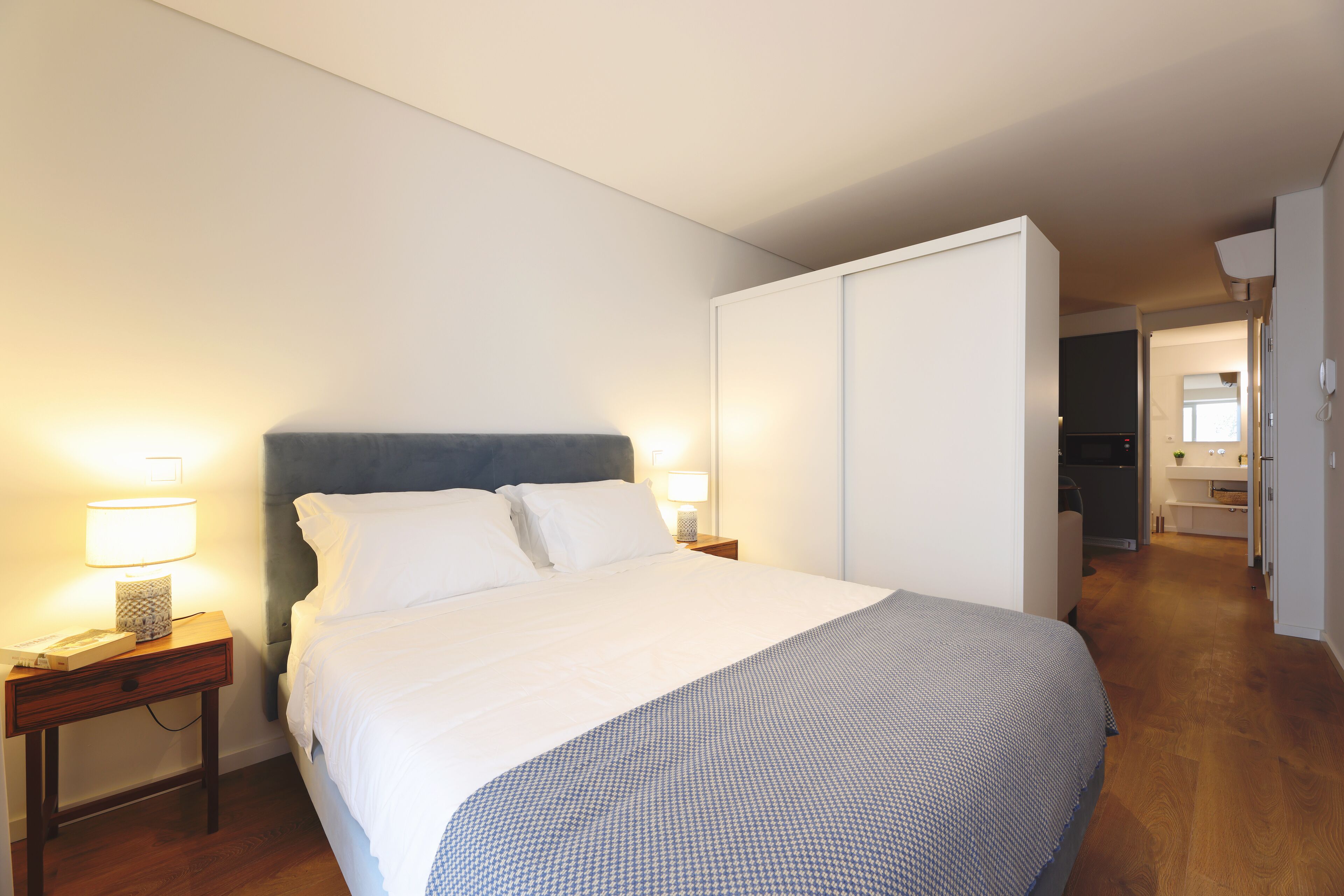 A neatly made bed with white linens, a dark headboard, and a bedside table with a lamp.