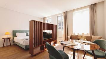 A hotel room with a bed, a TV, a dining table with chairs, and a sofa.