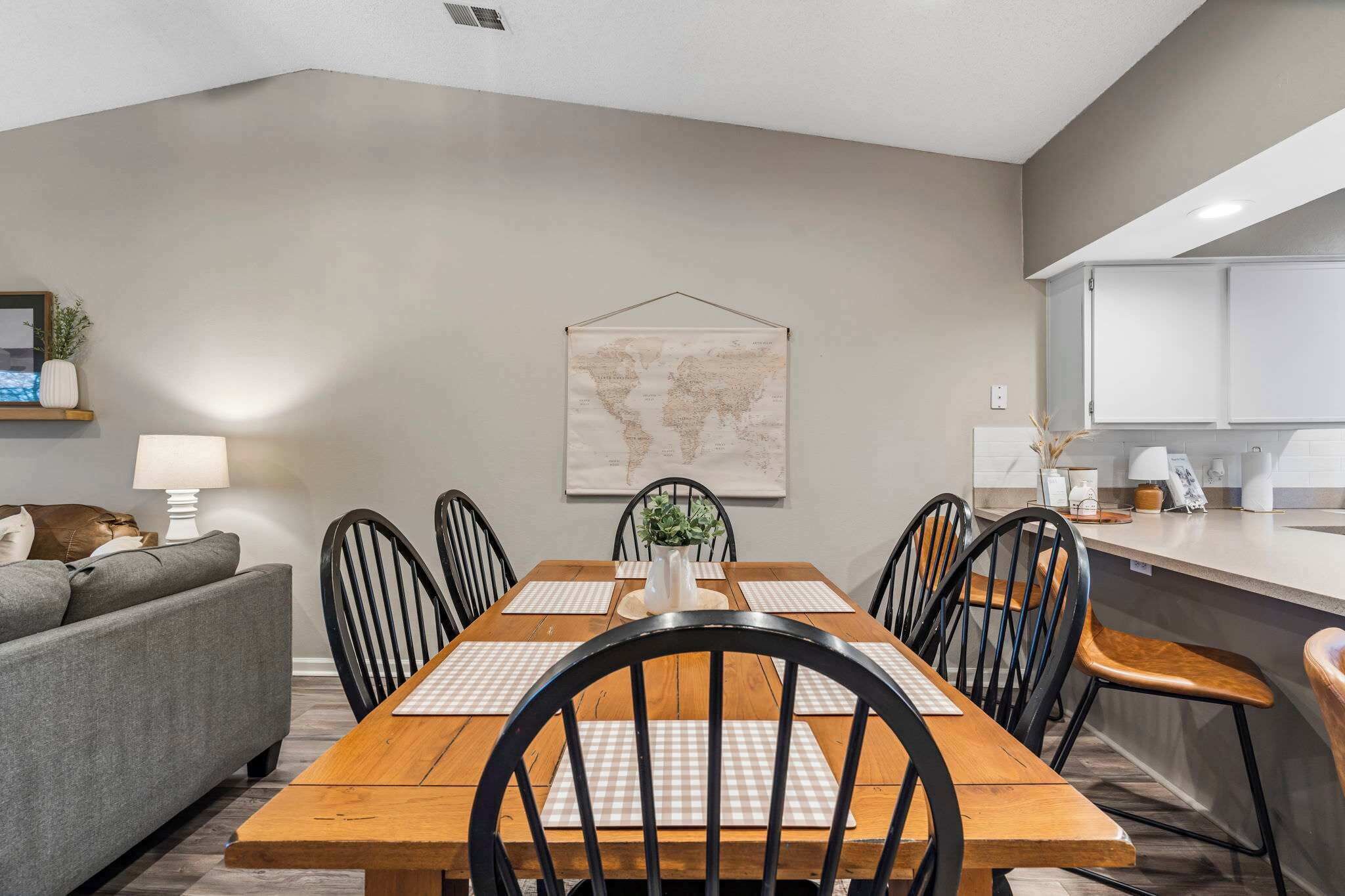 A modern dining area with a wooden table and black chairs, a grey sofa, and a world map on the wall.