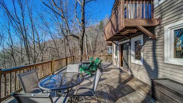 A deck with outdoor furniture, a glass table, and a view of trees.
