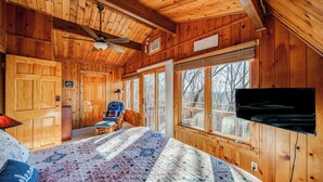 Un dormitorio de cabaña de madera acogedor, con una cama, un sillón, un televisor y ventanas amplias.