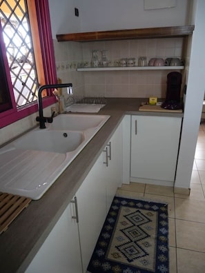 A kitchen with a double sink, a coffee maker, and a shelf with glassware.