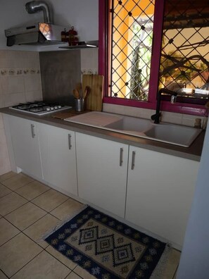 A kitchen with a gas stove, sink, and window with a view. - Appartement cozy en résidence (Libreville)