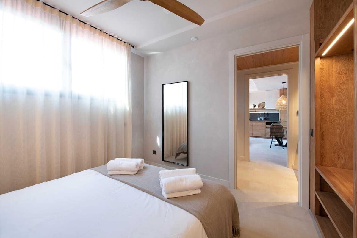 A hotel room with a large bed, a mirror, and a view into the kitchen area.