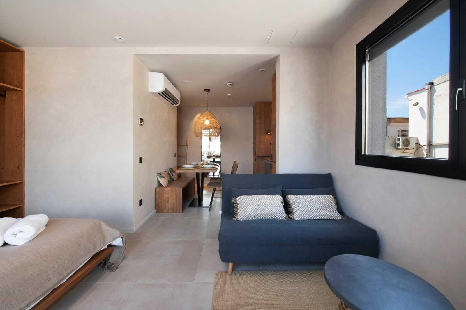 A modern, well-lit room with a sofa, a dining area, and a large window.