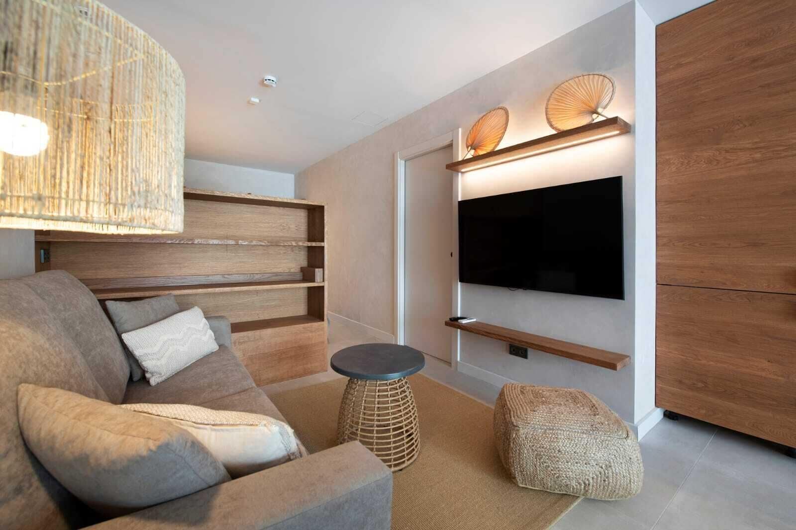 Un salon moderne doté d’un grand téléviseur à écran plat fixé au mur, d’étagères en bois, d’un canapé confortable et d’une table basse ronde.