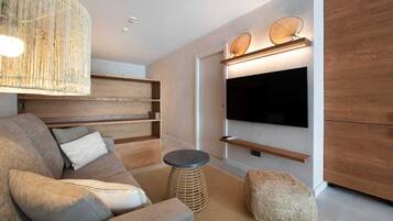 Un salon moderne doté d’un grand téléviseur à écran plat fixé au mur, d’étagères en bois, d’un canapé confortable et d’une table basse ronde.