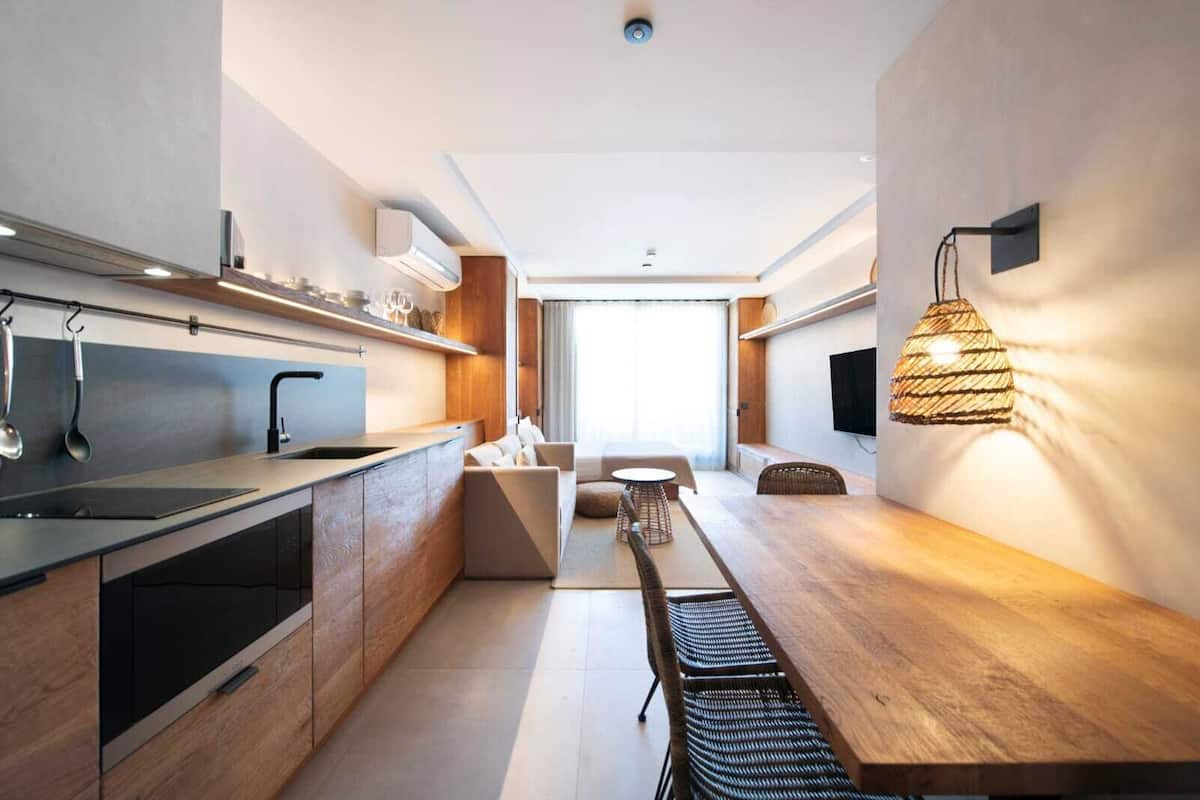 A modern kitchen with a central island, a dining area with a wooden table, and a living space with a sofa and TV.