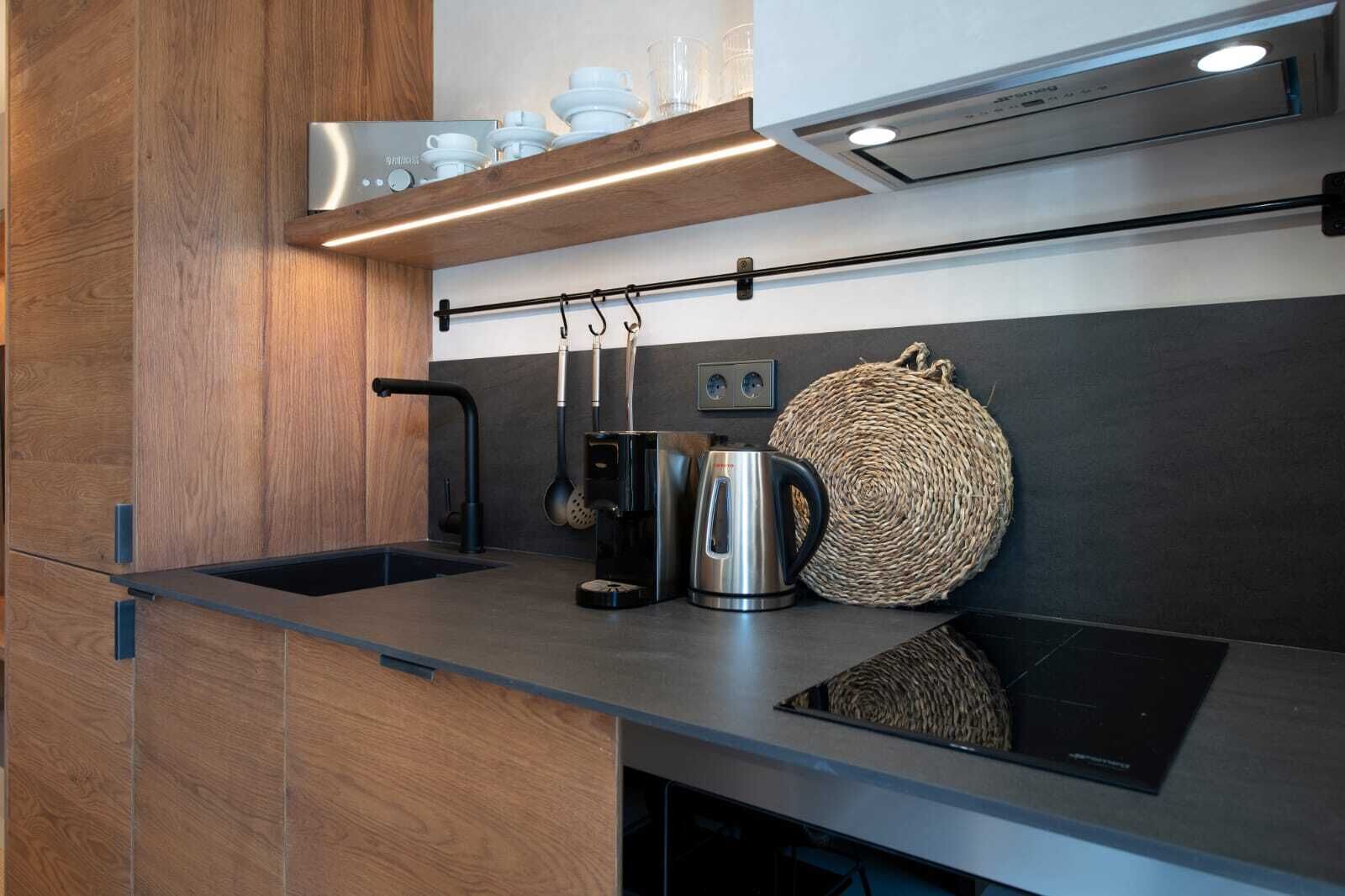 A modern kitchen with a black countertop, stainless steel kettle, and a woven basket.