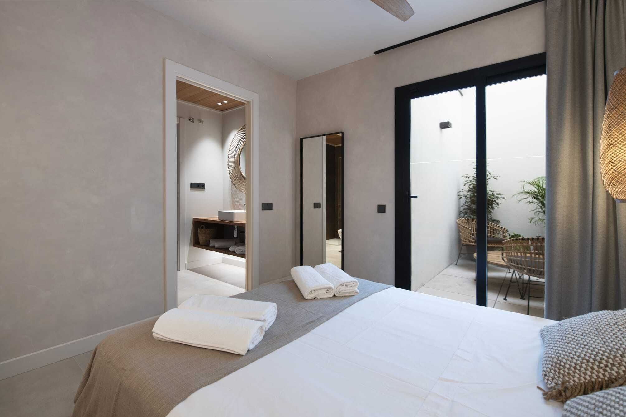 Een moderne slaapkamer met een groot bed, een badkamer met spiegel en een balkon met rieten meubilair.