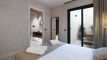 A modern bedroom with a large bed, a bathroom with a mirror, and a balcony with wicker furniture.