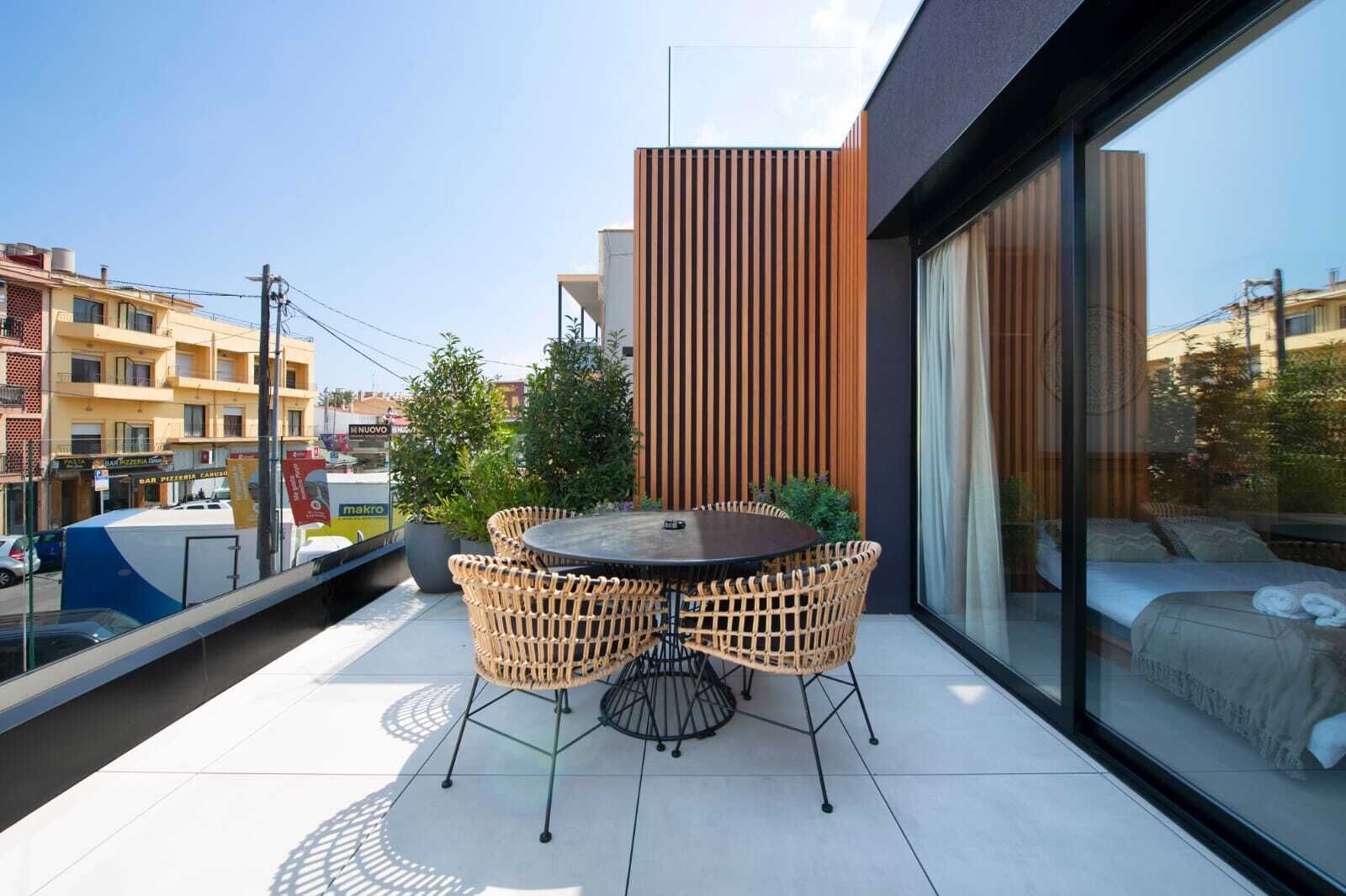 Een modern balkon met een ronde tafel en rieten stoelen, met uitzicht op een stadsgezicht.