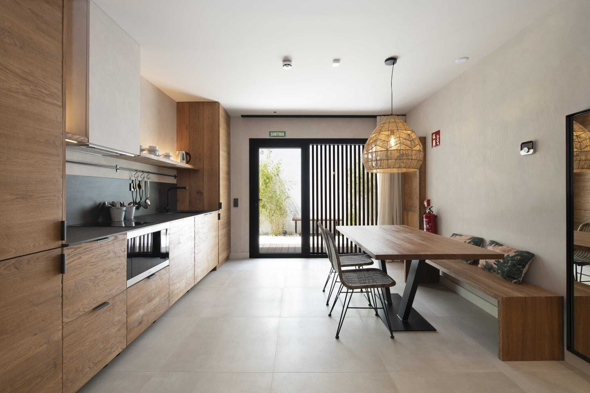 A modern kitchen with wooden cabinets, a black countertop, and a dining area with a wooden table and chairs.