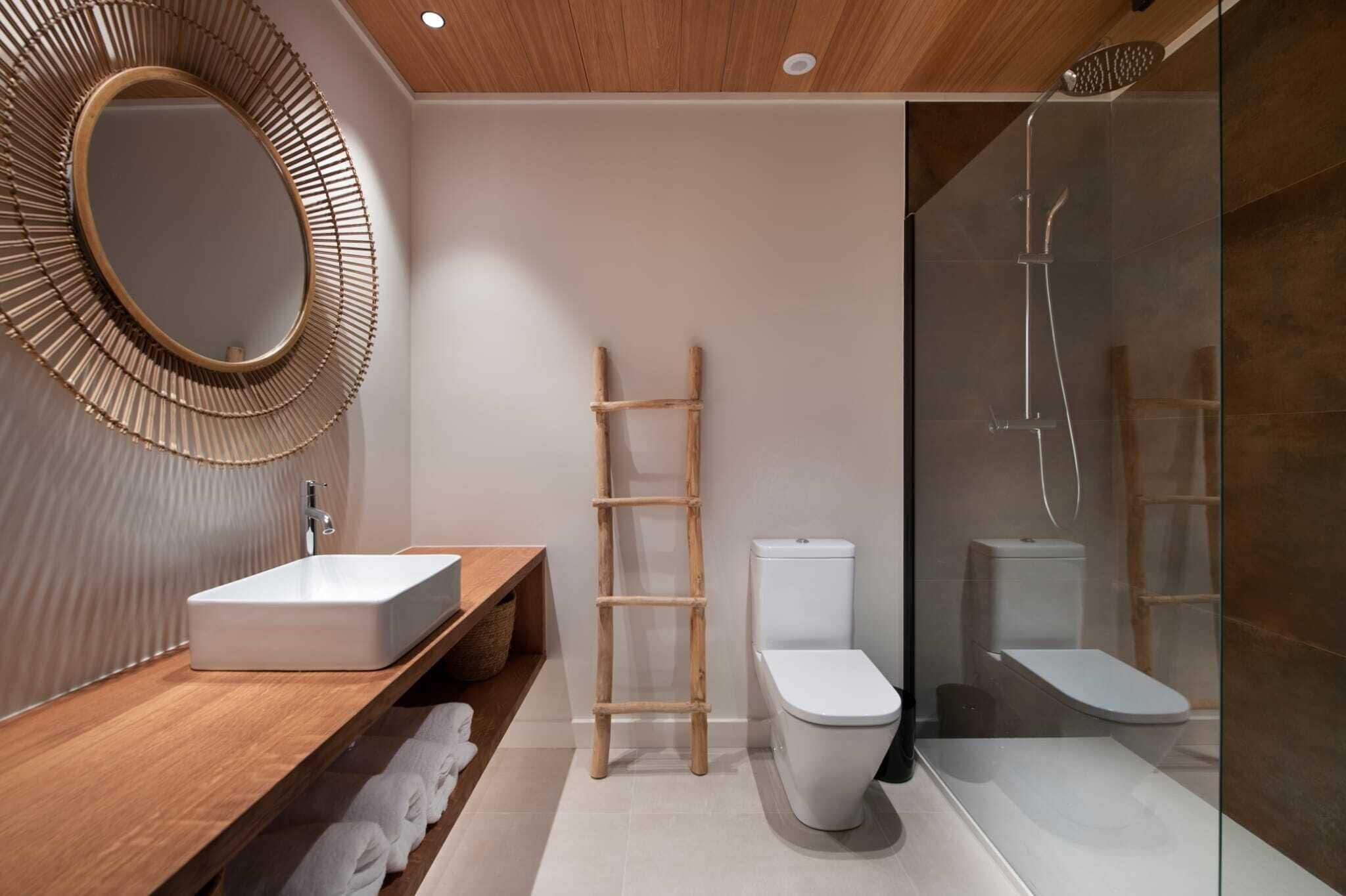 A modern bathroom with a wooden vanity, a freestanding toilet, a glass-enclosed shower, and a wooden ladder.