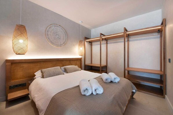 A modern hotel room with a large bed, a wooden headboard, a built-in wardrobe, and a decorative wall hanging.