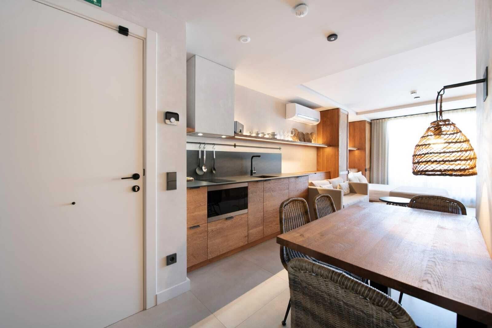 A modern kitchen with a wooden countertop, built-in oven, and a dining area with wicker chairs.