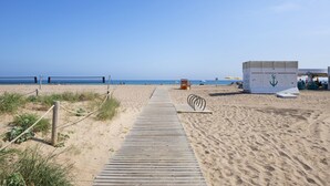 A sandy beach with a wooden boardwalk leading to a lifeguard station and beach umbrellas. - Apartamentos Balisse (Castelldefels)